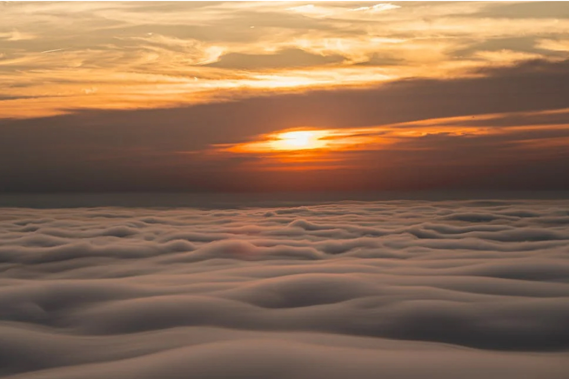 A warm orange sunset above a thick blanket of low cloud.