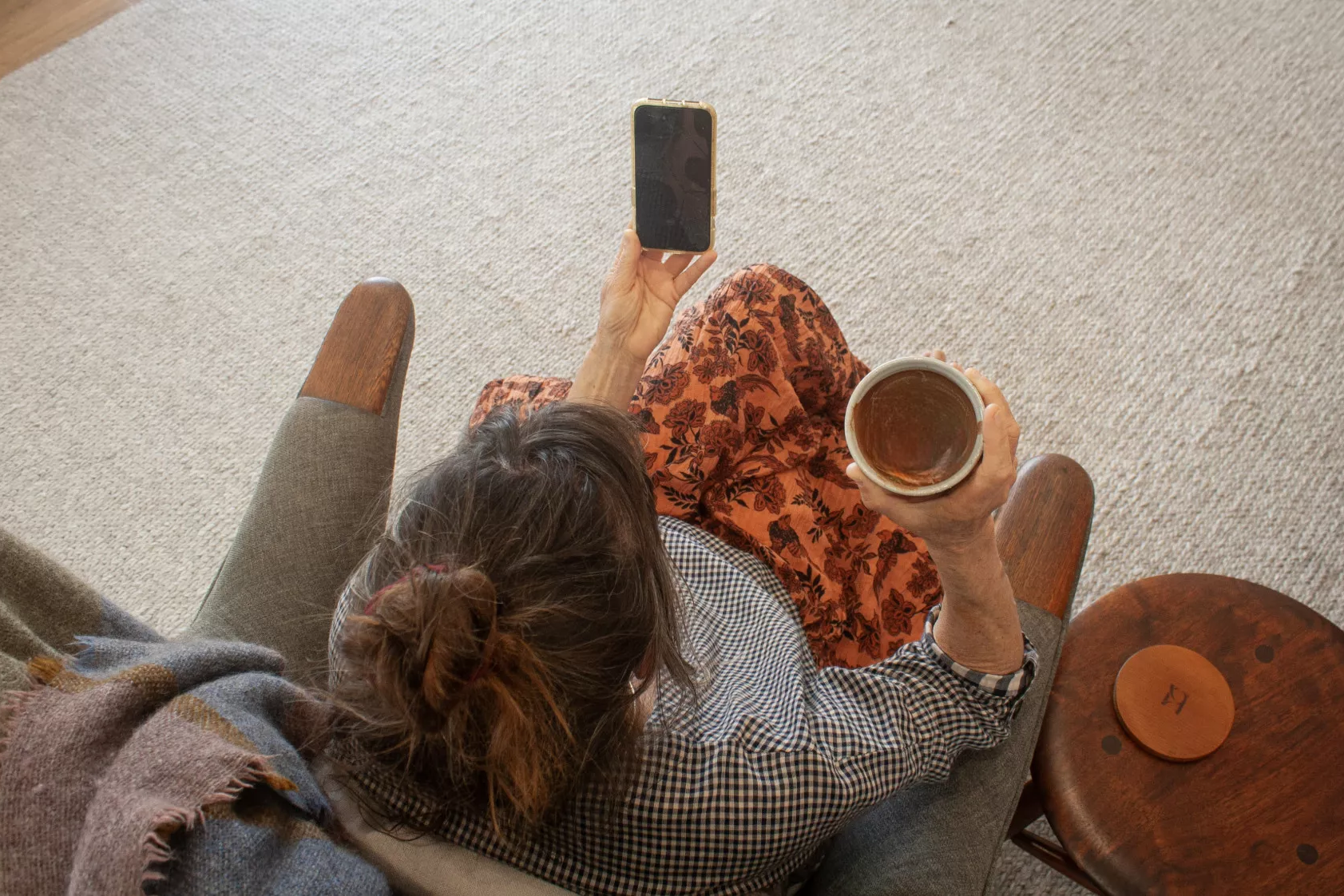 woman sits in a cosy chair with a cup of cacao in hand looking at her phone in an empathy angels session and feeling heard