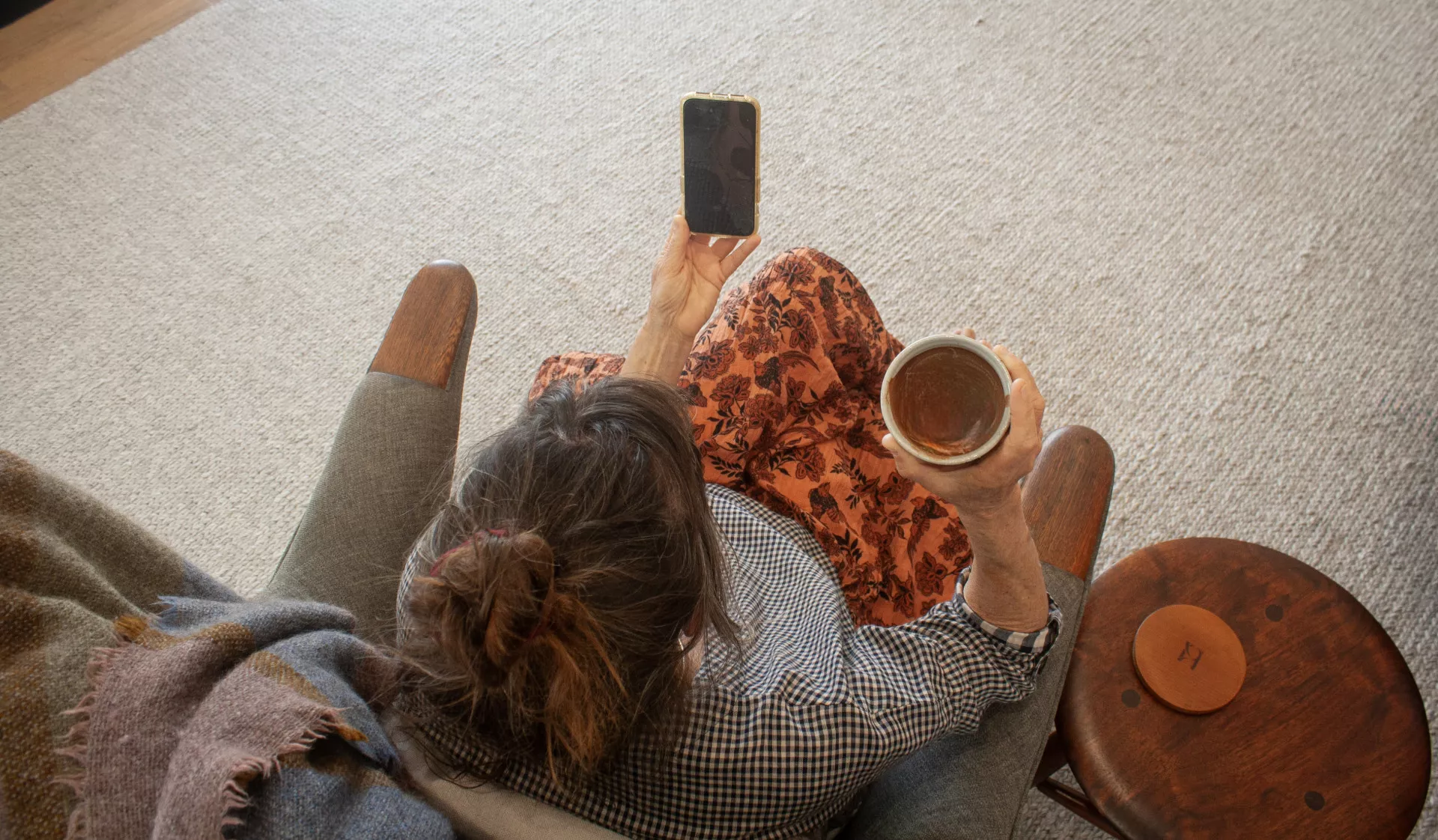 woman sits in a cosy chair with a cup of cacao in hand looking at her phone in an empathy angels session and feeling heard